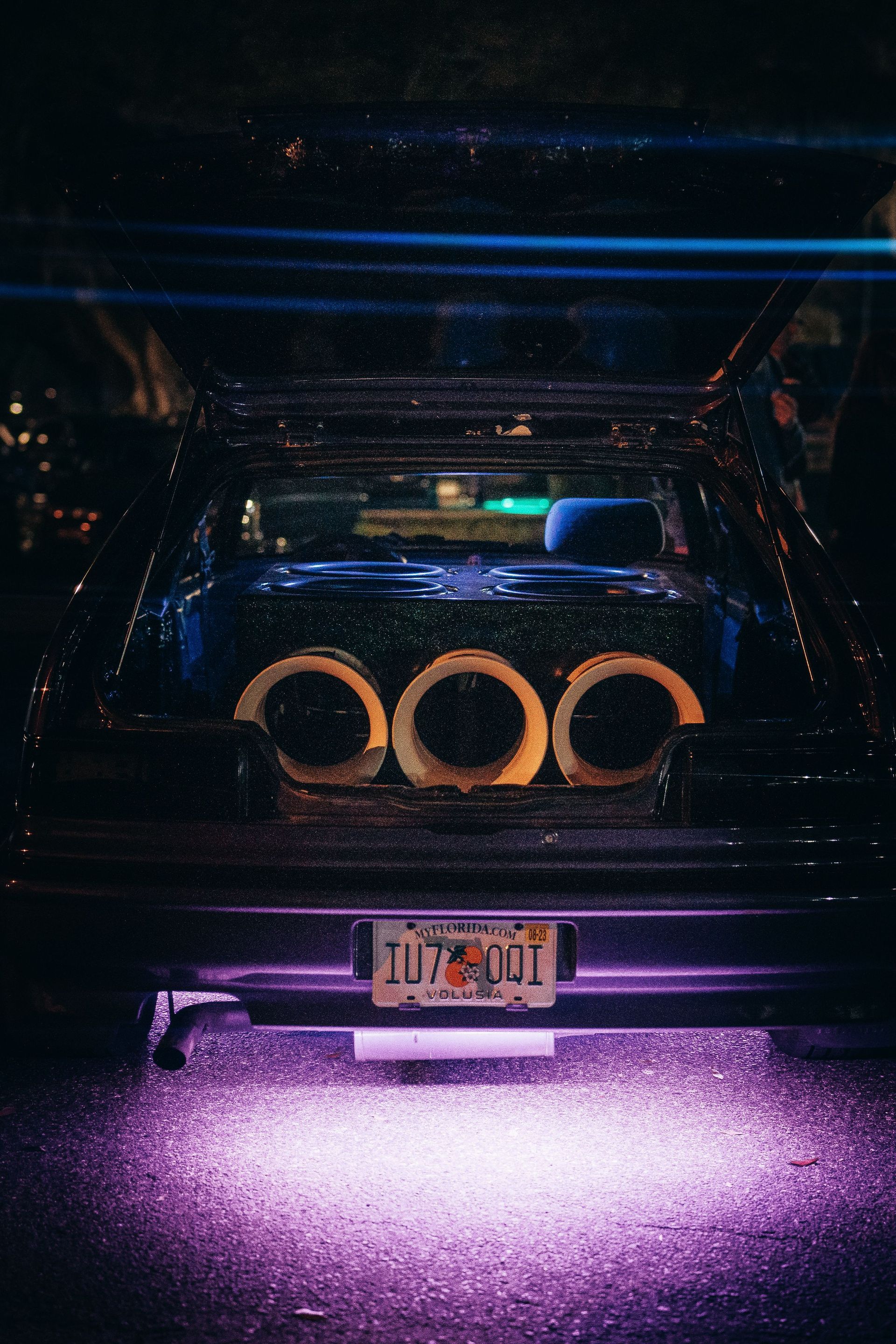 A modified car trunk featuring a powerful sound system with neon underglow lighting at night.